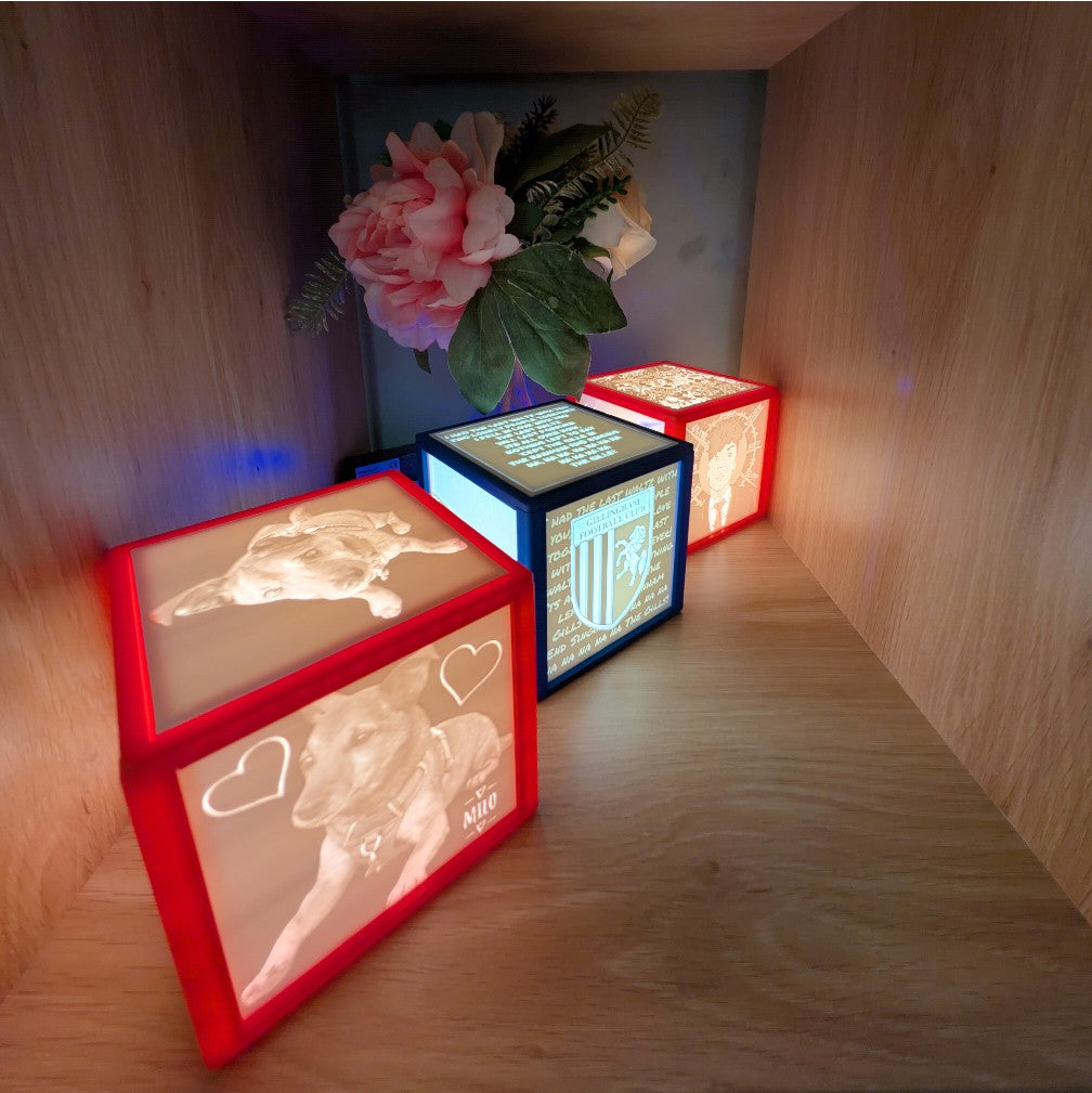 Three illuminated cube light boxes on a wooden surface with decorative elements. light box with four personalised photos.